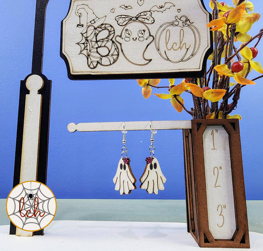 Handmade Halloween ghost dangle earrings displayed on a wooden stand with fall foliage decoration