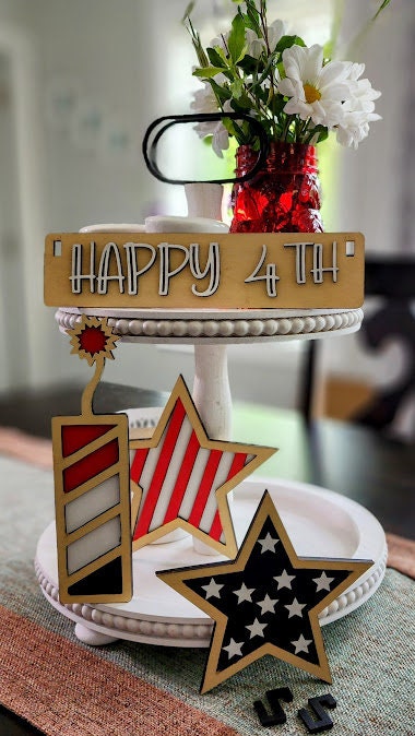 Wooden 4th of July decor insert featuring stars and stripes next to a Happy 4th sign on a white tiered tray