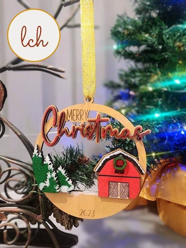 Wooden Merry Christmas ornament with red barn and green trees hanging on gold ribbon
