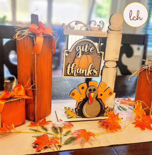 Wooden sign post insert with a turkey and give thanks message, surrounded by autumn leaves and orange wooden pumpkins