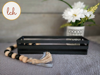 Black wooden wagon insert tray for organizing items, displayed on gray fabric with decorative beads and white flowers