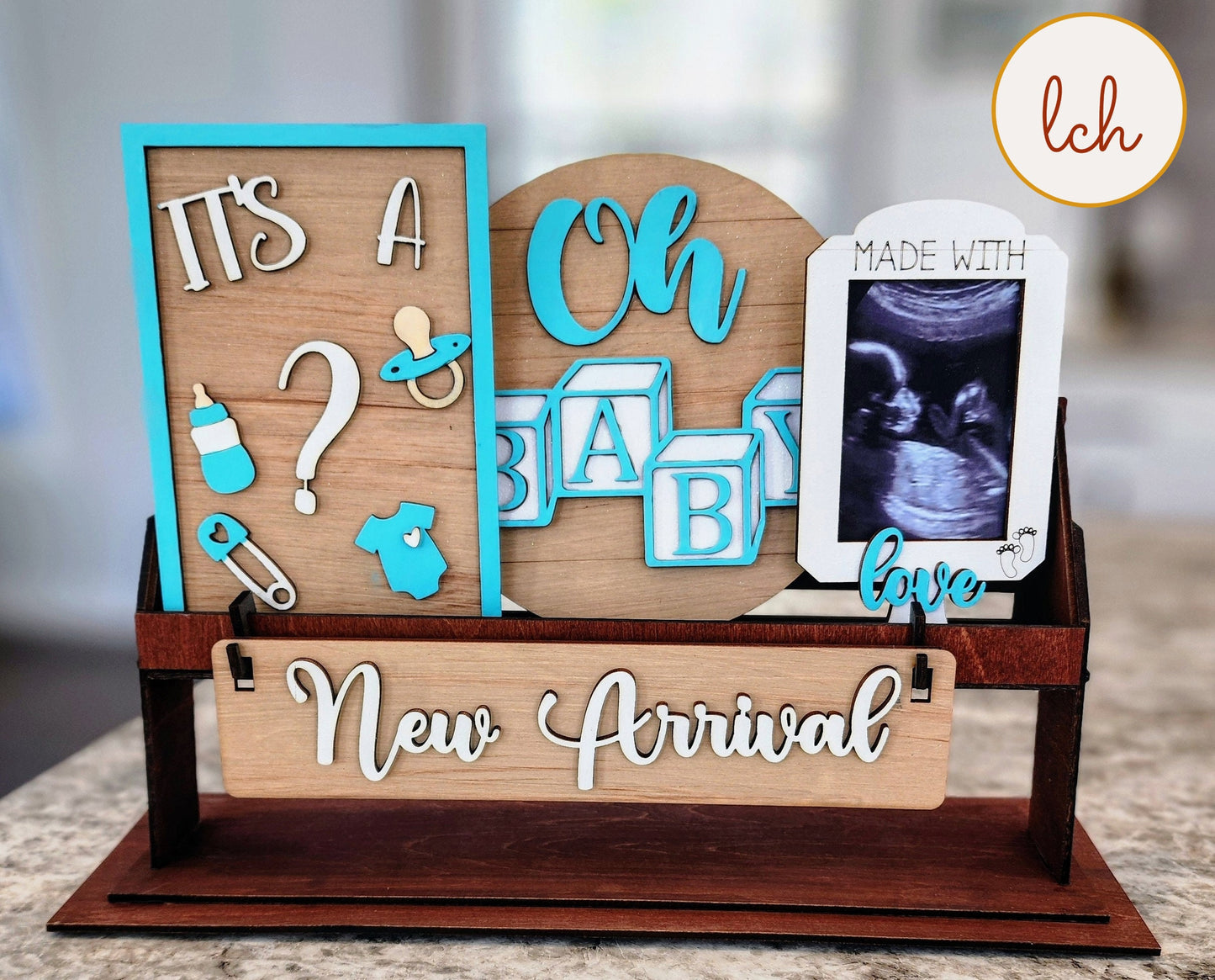 Wooden wagon insert with baby-themed decorations including pacifier, bottle, ultrasound frame, and New Arrival sign