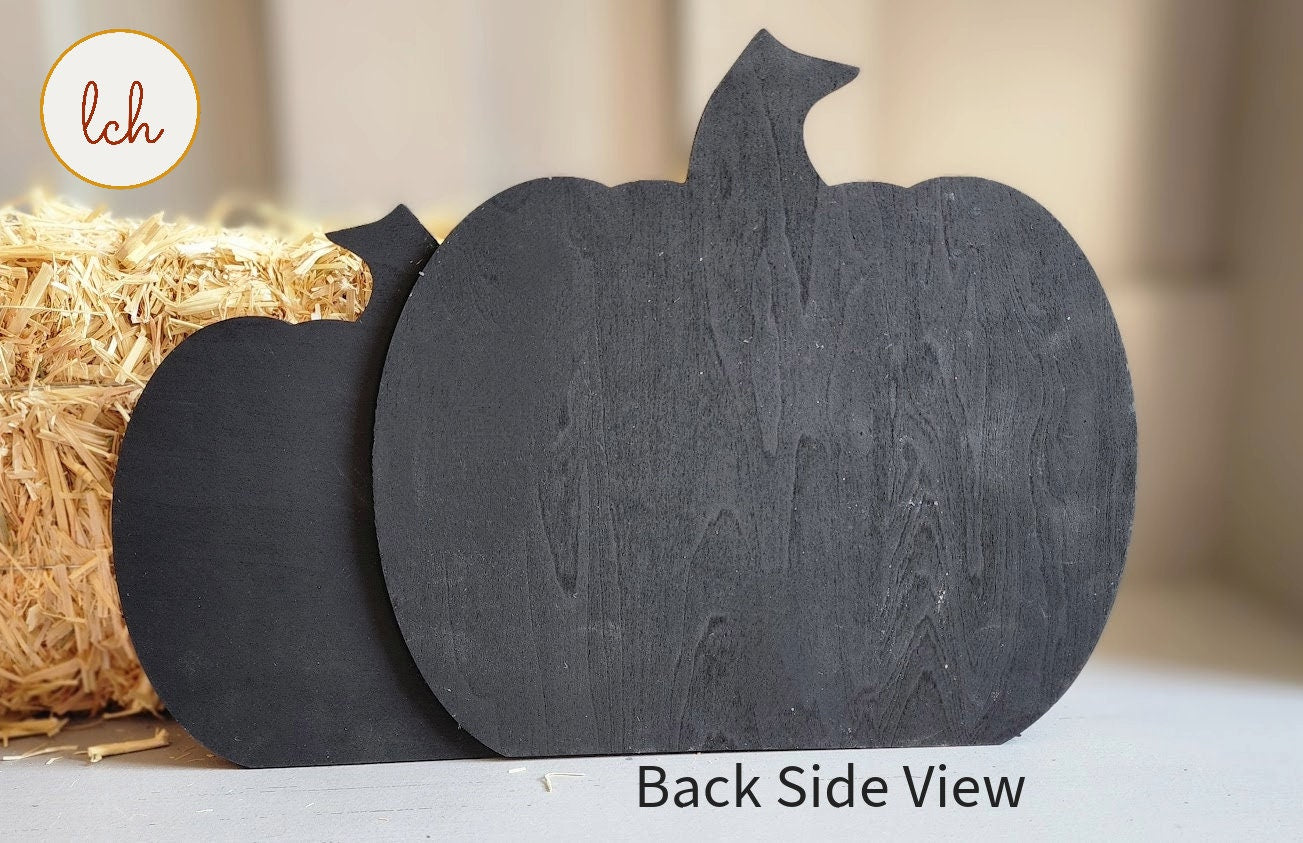Black wooden pumpkin sign with back side view next to a bale of straw for seasonal decor
